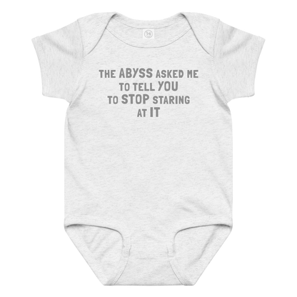 "The Abyss asked me to tell you to stop staring at it" printed on a ash baby jersey bodysuit laying on a flat surface amongst other clothes