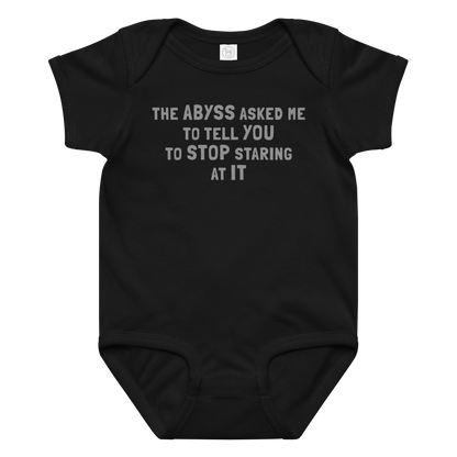 "The Abyss asked me to tell you to stop staring at it" printed on a black baby jersey bodysuit laying on a flat surface amongst other clothes