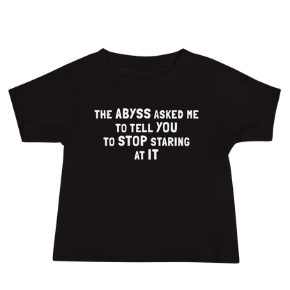 "The Abyss asked me to tell you to stop staring at it" printed on a black baby jersey short sleeve tee laying on a flat surface