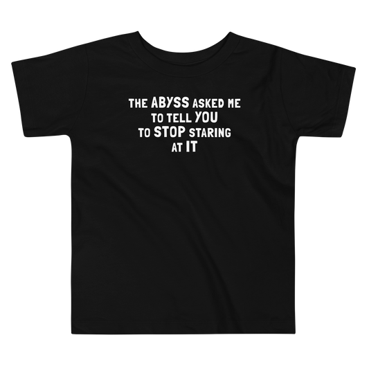 "The Abyss asked me to tell you to stop staring at it" printed on a black toddler short sleeve tee laying on a flat surface