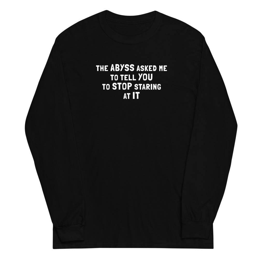 "The Abyss asked me to tell you to stop staring at it" printed on a black men's long sleeve shirt laying on a flat surface