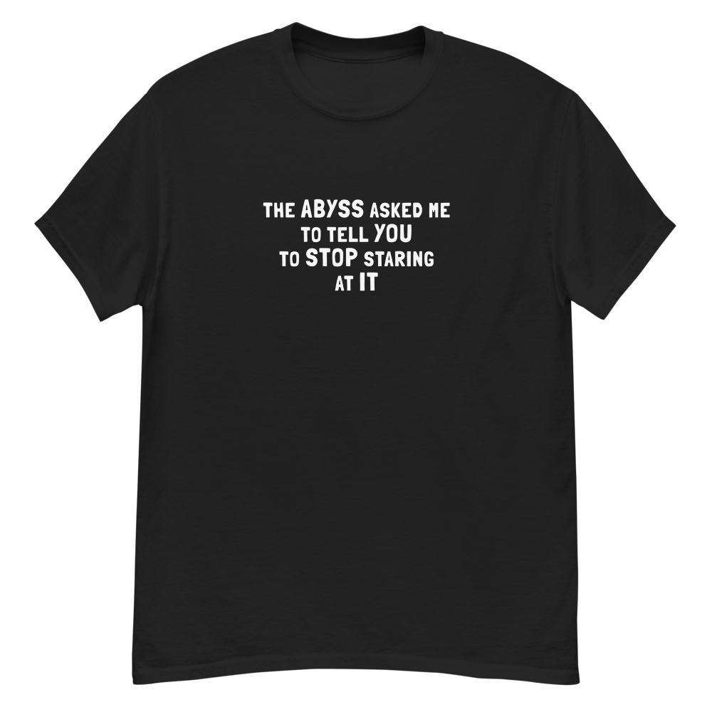 "The Abyss asked me to tell you to stop staring at it" printed on a black unisex classic tee laying on a flat surface