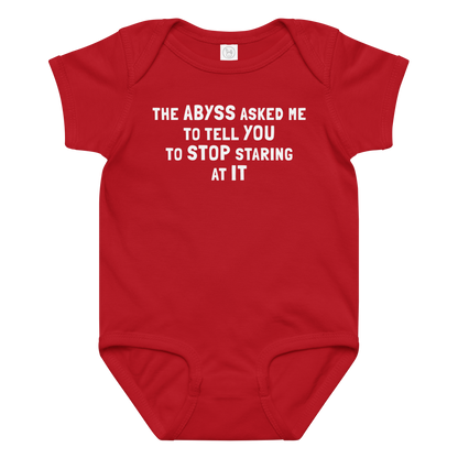 "The Abyss asked me to tell you to stop staring at it" printed on a red baby jersey bodysuit laying on a flat surface amongst other clothes