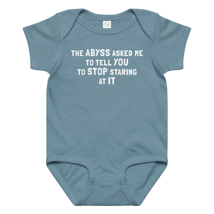 "The Abyss asked me to tell you to stop staring at it" printed on a vintage indigo baby jersey bodysuit laying on a flat surface amongst other clothes