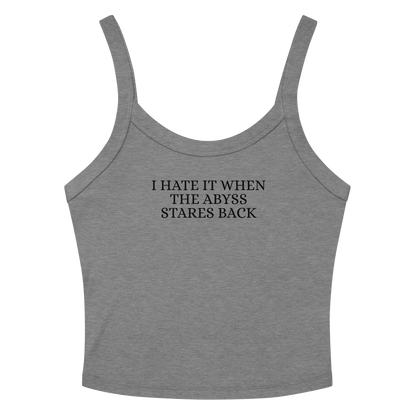 "I hate it when the abyss stares back" printed on a athletic heather women's micro-rib tanktop laying on a flat surface amongst sunglasses and shorts