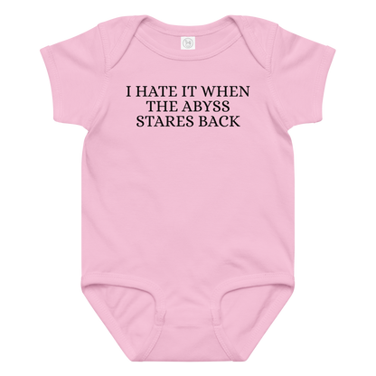"I hate it when the abyss stares back" printed on a pink baby jersey bodysuit laying on a flat surface amongst other clothes