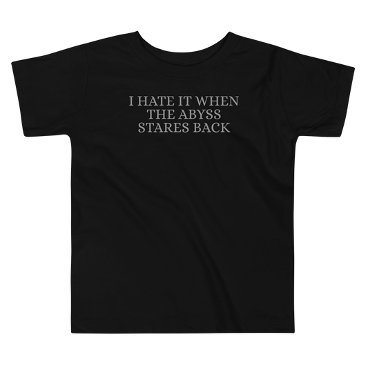 "I hate it when the abyss stares back" printed on a black toddler short sleeve tee laying on a flat surface