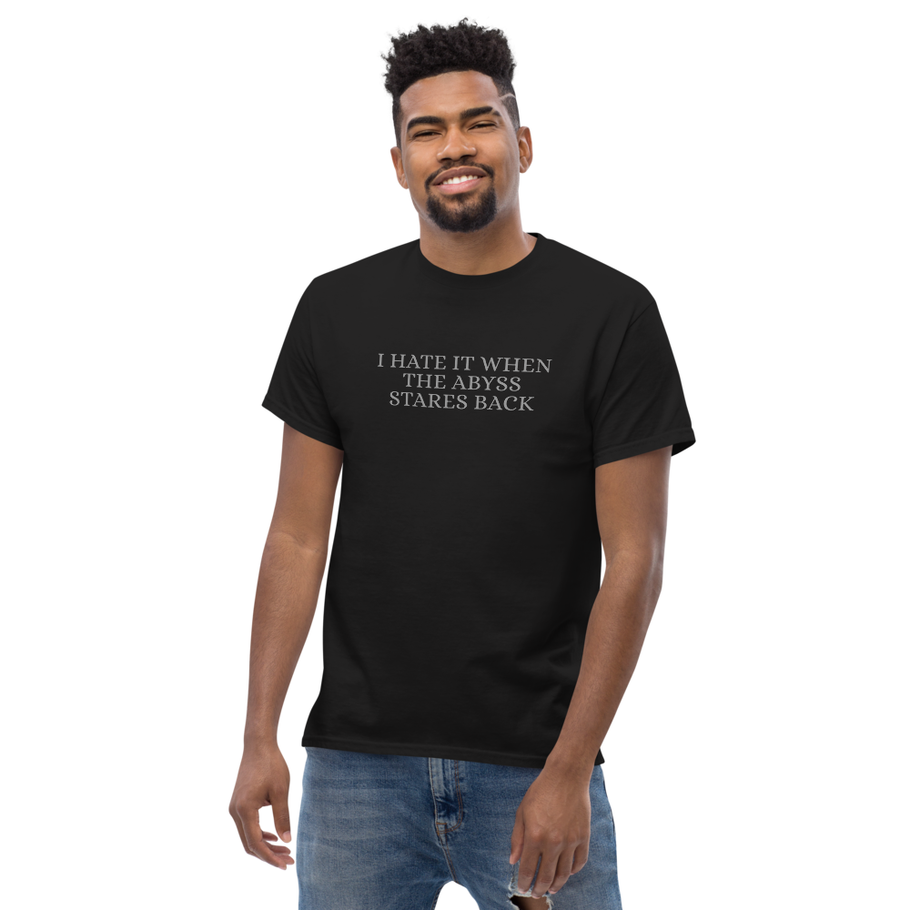 "I hate it when the abyss stares back" printed on a black unisex classic tee worn by a male