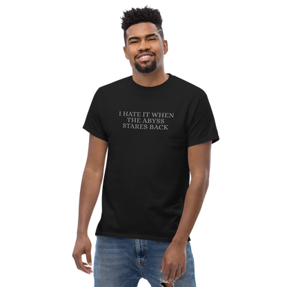 "I hate it when the abyss stares back" printed on a black unisex classic tee worn by a male