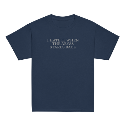 "I hate it when the abyss stares back" printed on a navy youth classic tee laying on a flat surface