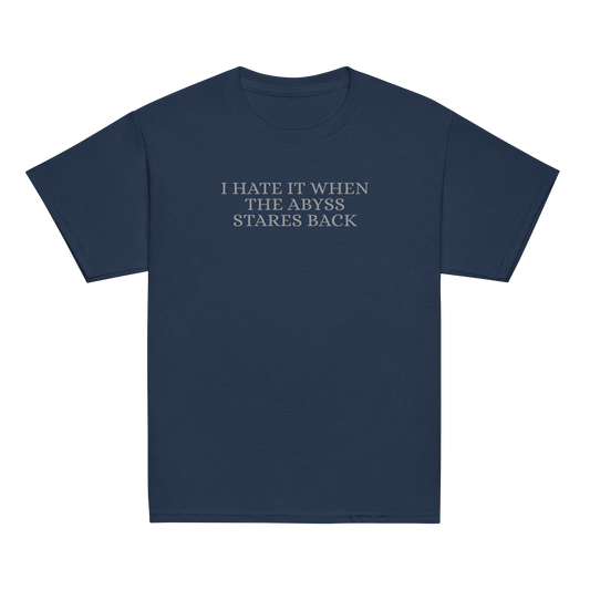 "I hate it when the abyss stares back" printed on a navy youth classic tee laying on a flat surface