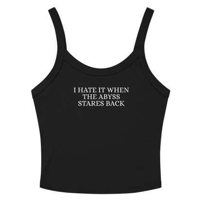 "I hate it when the abyss stares back" printed on a solid black blend women's micro-rib tanktop laying on a flat surface amongst sunglasses and shorts
