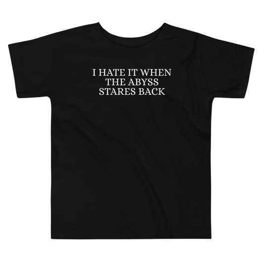 "I hate it when the abyss stares back" printed on a black toddler short sleeve tee laying on a flat surface