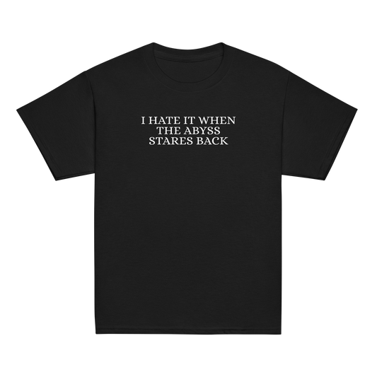"I hate it when the abyss stares back" printed on a black youth classic tee laying on a flat surface