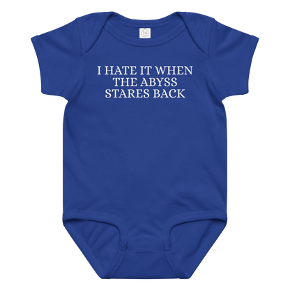 "I hate it when the abyss stares back" printed on a royal baby jersey bodysuit laying on a flat surface amongst other clothes