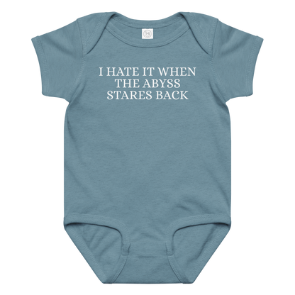 "I hate it when the abyss stares back" printed on a vintage indigo baby jersey bodysuit laying on a flat surface amongst other clothes