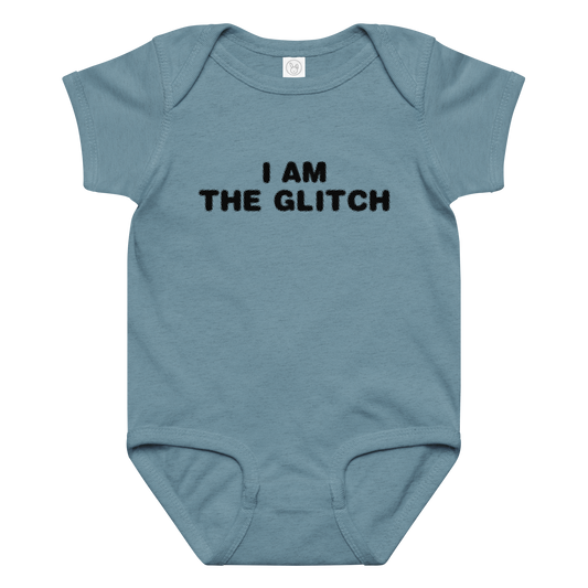 "I am the glitch" printed on a vintage indigo baby jersey bodysuit laying on a flat surface amongst other clothes