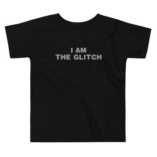 "I am the glitch" printed on a black toddler short sleeve tee laying on a flat surface