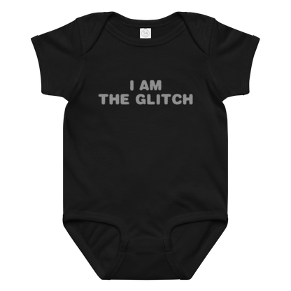 "I am the glitch" printed on a black baby jersey bodysuit laying on a flat surface amongst other clothes