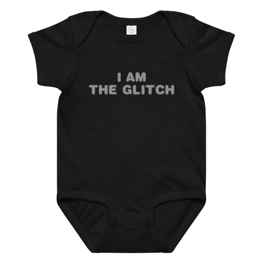 "I am the glitch" printed on a black baby jersey bodysuit laying on a flat surface amongst other clothes