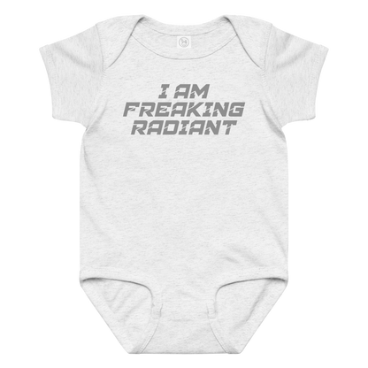 "I Am Freaking Radiant" printed on a ash baby jersey bodysuit laying on a flat surface amongst other clothes
