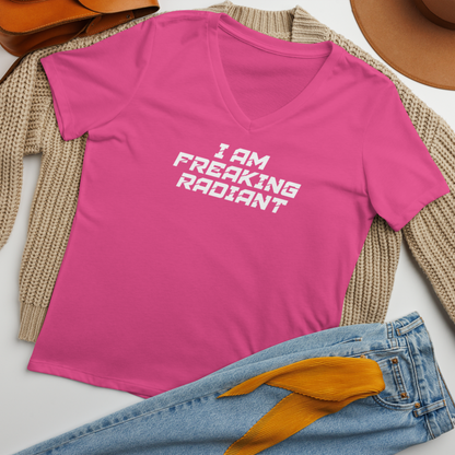 "I Am Freaking Radiant" printed on a berry women's relaxed v-neck t-shirt laying on a flat surface amongst other clothes
