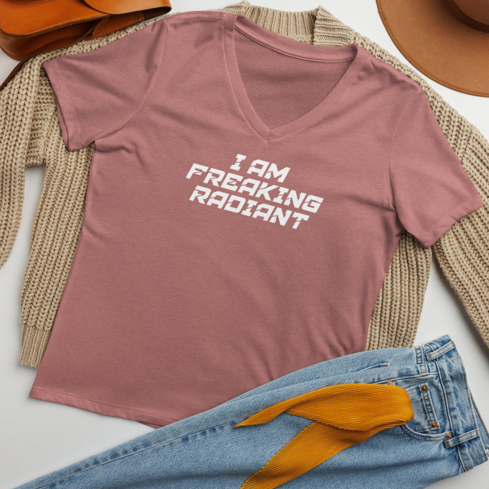 "I Am Freaking Radiant" printed on a heather mauve women's relaxed v-neck t-shirt laying on a flat surface amongst other clothes