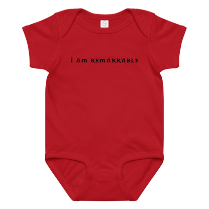 "I am remarkable" printed on a red baby jersey bodysuit laying on a flat surface amongst other clothes