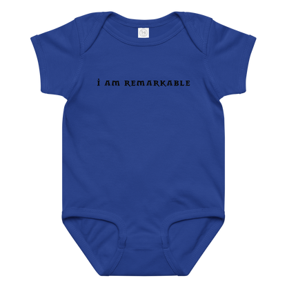 "I am remarkable" printed on a royal baby jersey bodysuit laying on a flat surface amongst other clothes