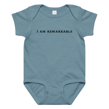 "I am remarkable" printed on a vintage indigo baby jersey bodysuit laying on a flat surface amongst other clothes