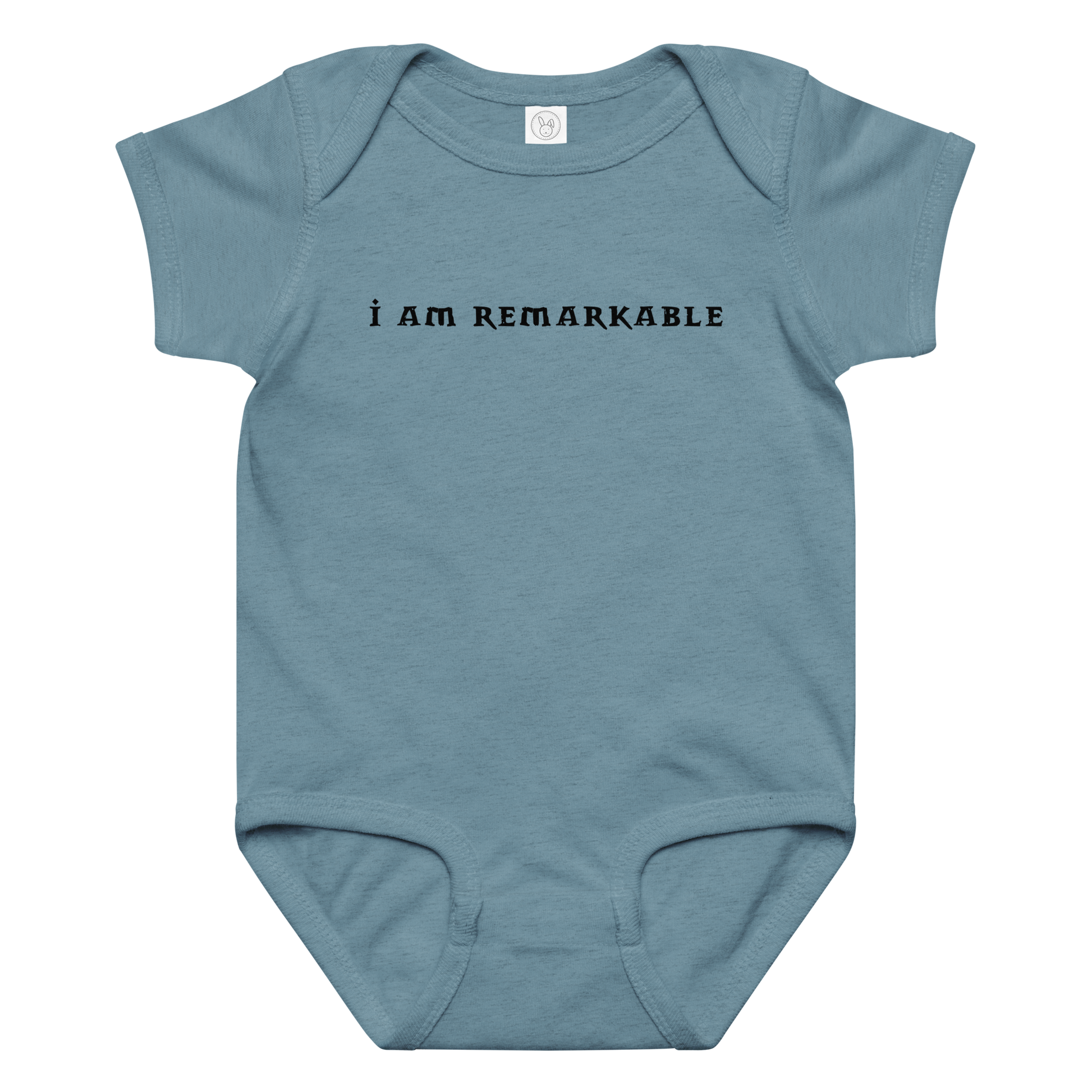"I am remarkable" printed on a vintage indigo baby jersey bodysuit laying on a flat surface amongst other clothes