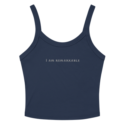 "I am remarkable" printed on a solid navy blend women's micro-rib tanktop laying on a flat surface amongst sunglasses and shorts