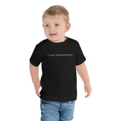 "I am remarkable" printed on a black toddler short sleeve tee worn by a male