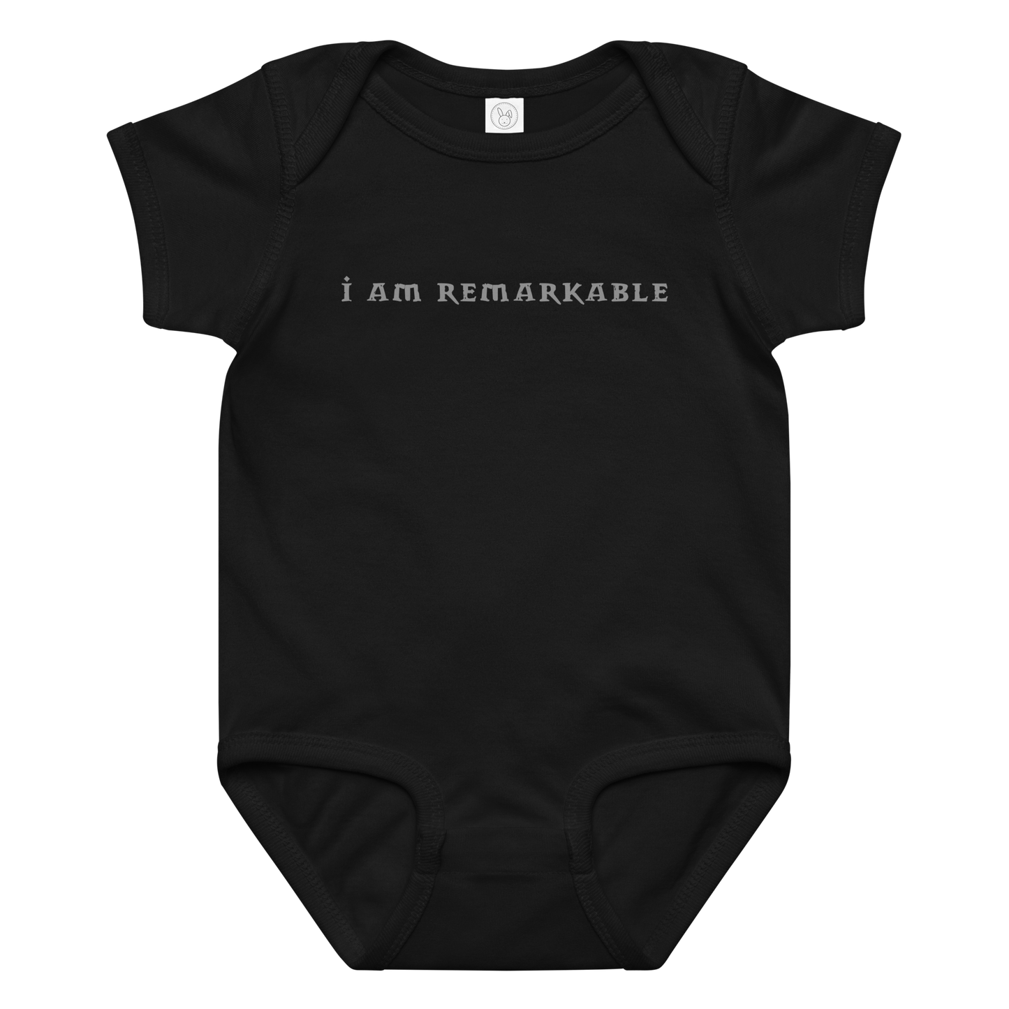 "I am remarkable" printed on a black baby jersey bodysuit laying on a flat surface amongst other clothes