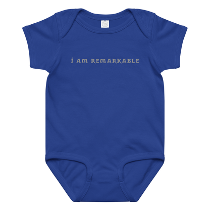 "I am remarkable" printed on a royal baby jersey bodysuit laying on a flat surface amongst other clothes