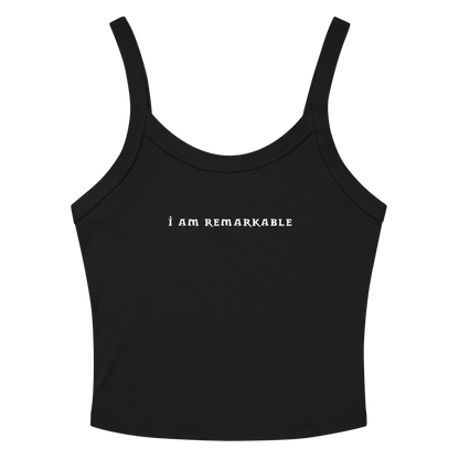 "I am remarkable" printed on a solid black blend women's micro-rib tanktop laying on a flat surface amongst sunglasses and shorts