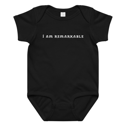 "I am remarkable" printed on a black baby jersey bodysuit laying on a flat surface amongst other clothes