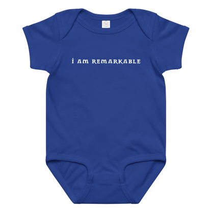 "I am remarkable" printed on a royal baby jersey bodysuit laying on a flat surface amongst other clothes