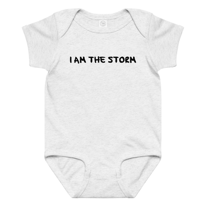 "I am the storm" printed on a ash baby jersey bodysuit laying on a flat surface amongst other clothes