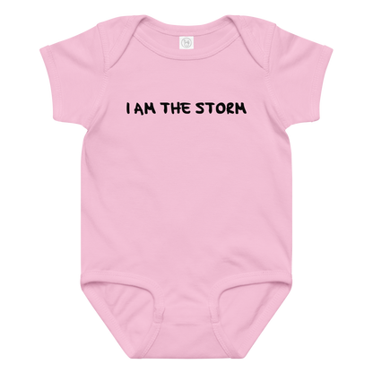 "I am the storm" printed on a pink baby jersey bodysuit laying on a flat surface amongst other clothes
