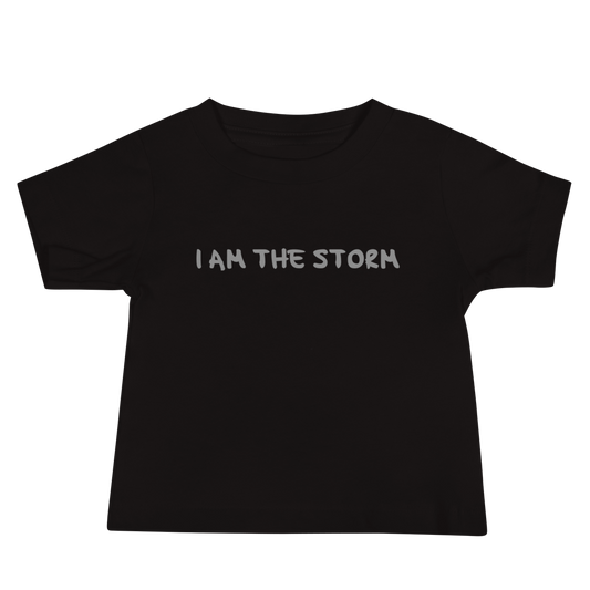 "I am the storm" printed on a black baby jersey short sleeve tee laying on a flat surface