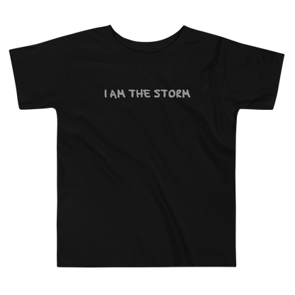 "I am the storm" printed on a black toddler short sleeve tee laying on a flat surface