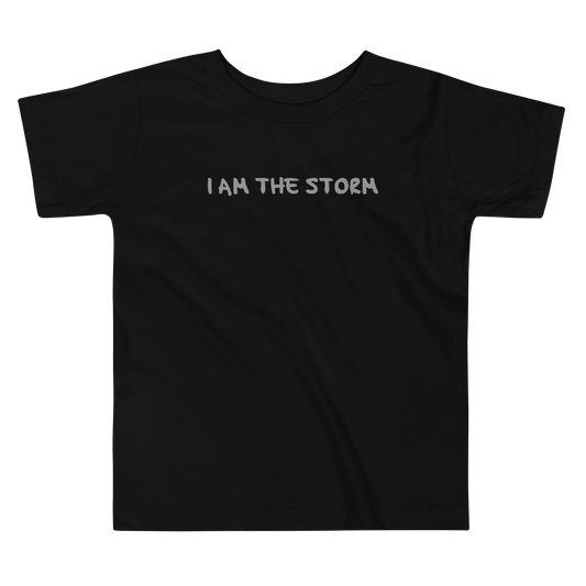 "I am the storm" printed on a black toddler short sleeve tee laying on a flat surface