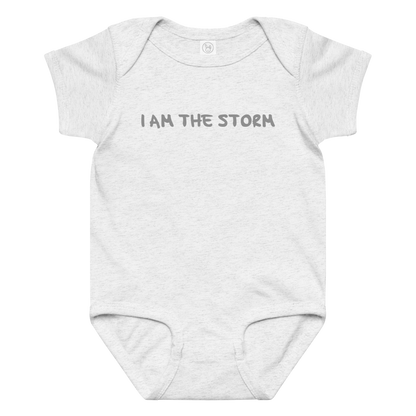 "I am the storm" printed on a ash baby jersey bodysuit laying on a flat surface amongst other clothes