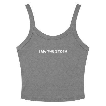"I am the storm" printed on a athletic heather women's micro-rib tanktop laying on a flat surface amongst sunglasses and shorts