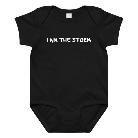 "I am the storm" printed on a black baby jersey bodysuit laying on a flat surface amongst other clothes