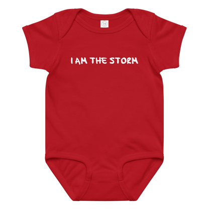 "I am the storm" printed on a red baby jersey bodysuit laying on a flat surface amongst other clothes