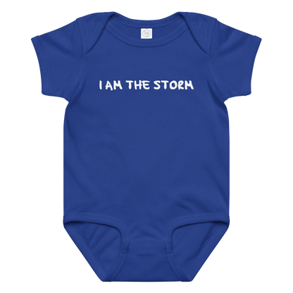 "I am the storm" printed on a royal baby jersey bodysuit laying on a flat surface amongst other clothes