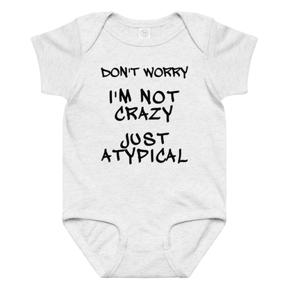 "Don't Worry I'm Not Crazy Just Atypical" printed on a ash baby jersey bodysuit laying on a flat surface amongst other clothes