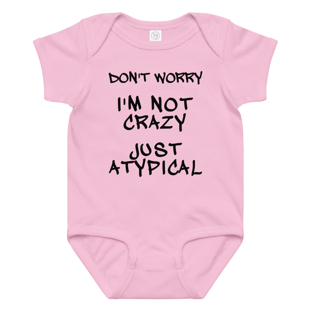 "Don't Worry I'm Not Crazy Just Atypical" printed on a pink baby jersey bodysuit laying on a flat surface amongst other clothes